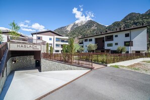 A modern residential building with a sign reading 'HASLACH RESIDENCE,' a paved driveway, and a mountain backdrop.