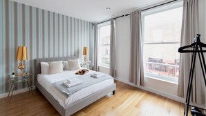 Une chambre d’hôtel moderne avec un grand lit, une petite table de chevet avec des lampes, une fenêtre avec des rideaux et une vue sur la ville.