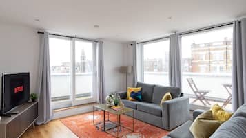 Una sala de estar moderna con un sofá gris, una mesa de centro y un televisor que muestra Netflix.