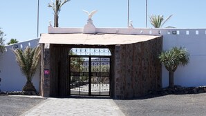 A gated entrance with a decorative top, a stone wall, and palm trees. - Apartment Siempreviva on Finca Falcon Cresta (Agüimes)