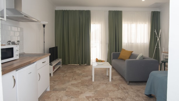 A compact living space with a kitchenette, a grey sofa, a small white table, and a dining area. - Apartment Siempreviva on Finca Falcon Cresta (Agüimes)