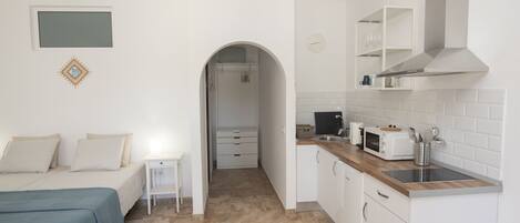 Una habitación con una cama, una mesita de noche pequeña, una kitchenette con microondas, tostadora y lavaplatos.
