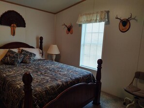 Quarto com uma cama grande, uma mesa de cabeceira com abajur, uma cadeira e chifres de veado fixados na parede.