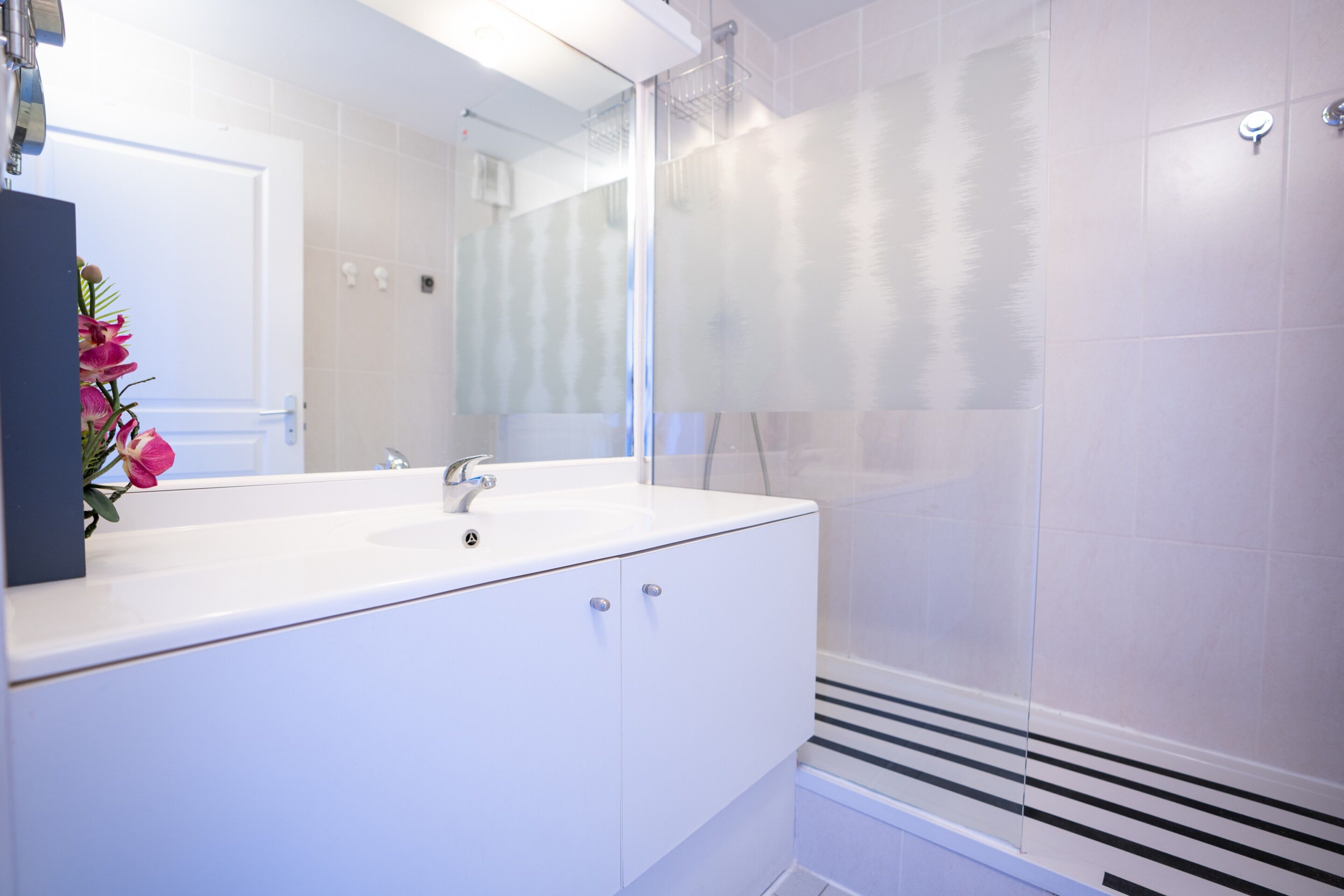 A modern bathroom with a white sink, mirror, and shower enclosure.