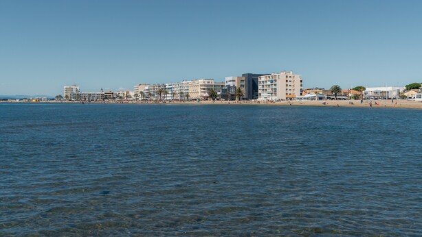Un hotel costero de varios pisos, con una playa al fondo y cielos despejados.