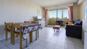 Un área de comedor con una mesa y sillas, un sofá, una mesita con mantel y una ventana con cortinas.