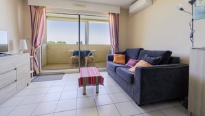 Una sala de estar con sofá, una mesita, televisor y un balcón con cortinas.
