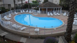 Una piscina circular con sillas de descanso blancas y una zona de terraza cercada.