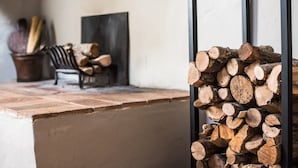 Ein Kamin mit Holzstapel, ein Sessel und ein Gemälde an der Wand.