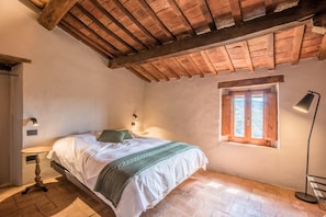 Quarto com cama, janela, luminária e uma pequena mesa.