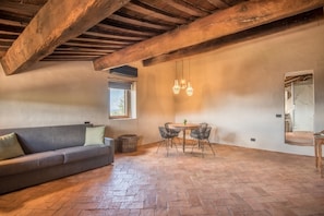 Quarto com teto de madeira, um sofá, uma mesa com cadeiras e uma janela.