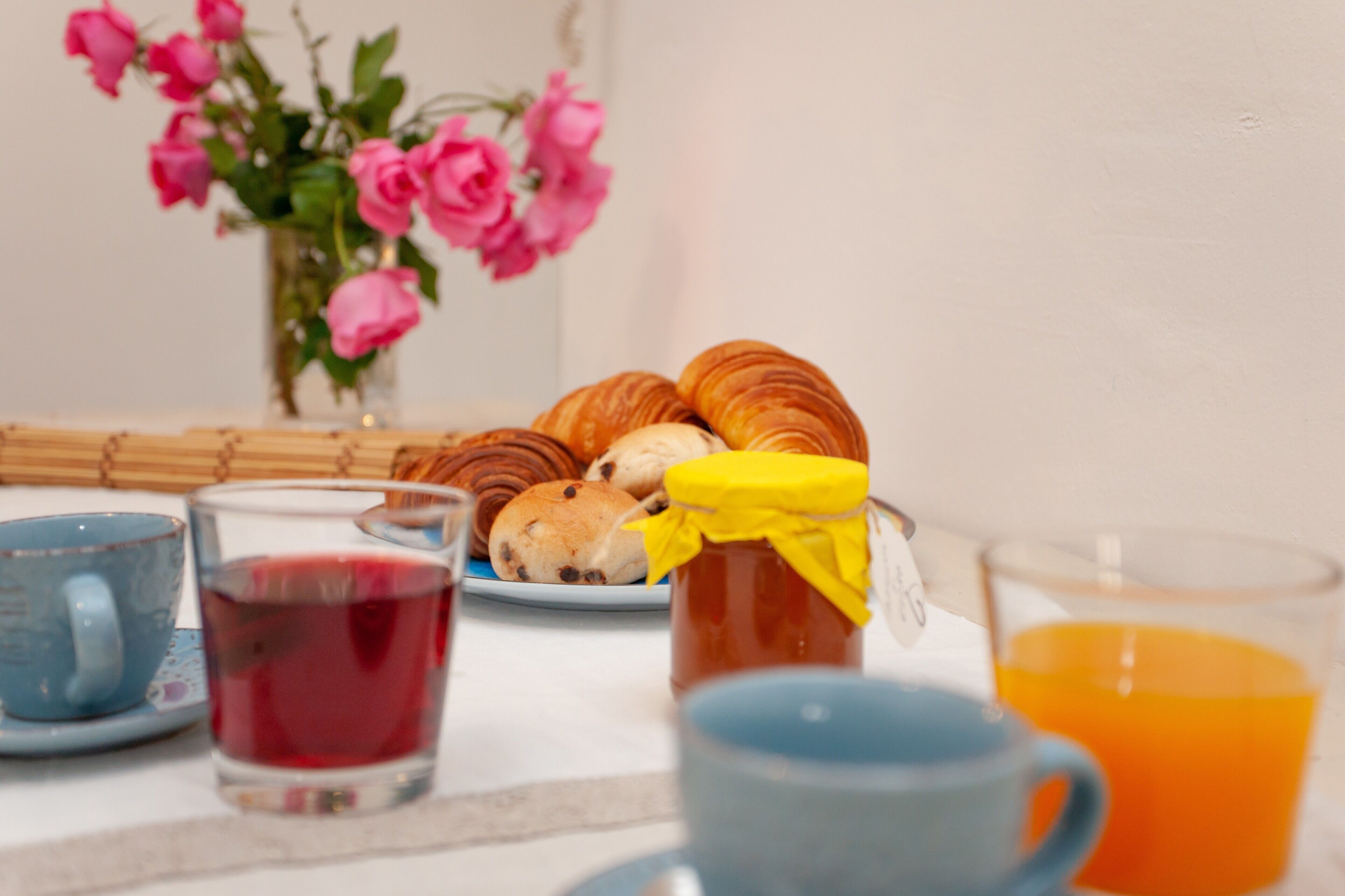 Une table mise pour le petit-déjeuner avec des viennoiseries, un pot de confiture et un verre de jus d’orange.