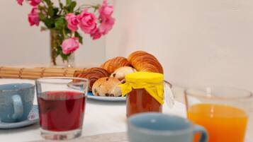 Une table mise pour le petit-déjeuner avec des viennoiseries, un pot de confiture et un verre de jus d’orange.