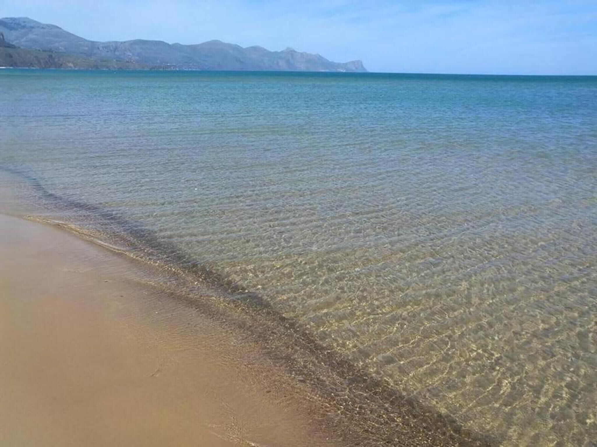Una playa con agua cristalina y montañas a lo lejos.