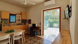 Una cuina compacta amb zona de menjador, ventilador de sostre i una porta corredissa de vidre que dona a un balcó.
