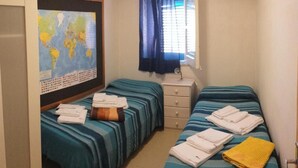 Habitació amb dos llits, un mapa a la paret, una finestra amb cortines i una taula de nit amb tovalloles.