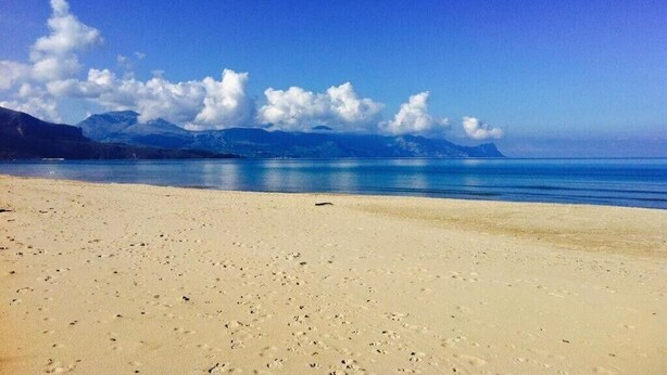 Una platja amb un cel clar i muntanyes al fons.
