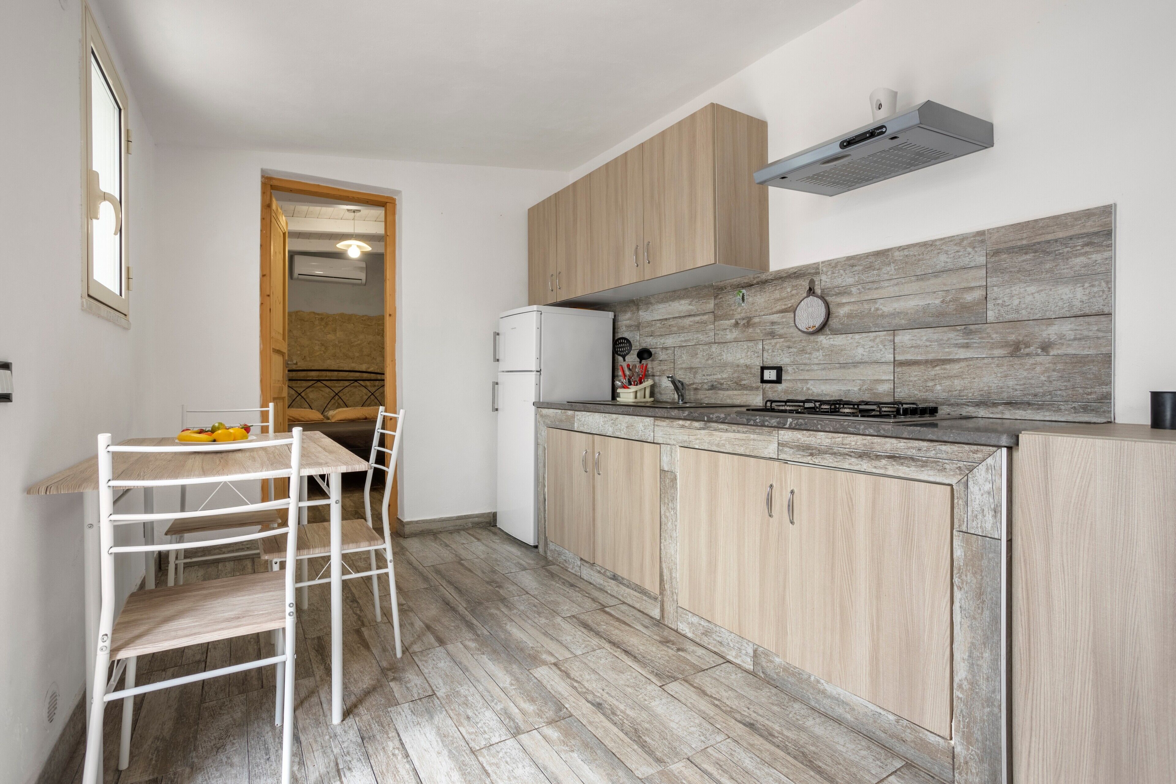 Une cuisine moderne avec des meubles en bois, une cuisinière encastrée et un coin repas comprenant une table et des chaises blanches.