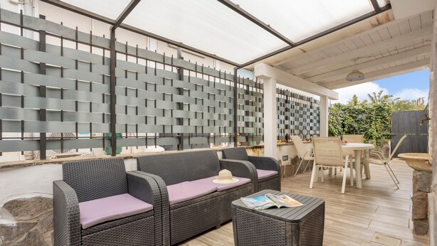 Un espace extérieur aménagé en terrasse, avec des meubles en osier, une table et un coin salon abrité.
