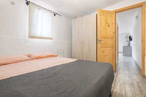 Une chambre à coucher comprenant un lit, une armoire, une fenêtre avec des rideaux et une porte donnant sur une autre pièce.