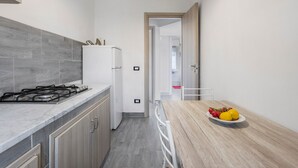 Et moderne køkken med gaskomfur, hvidt køleskab og et træbord med frugt.