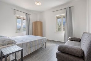 A room with a bed, a sofa, a wardrobe, and two windows with curtains.