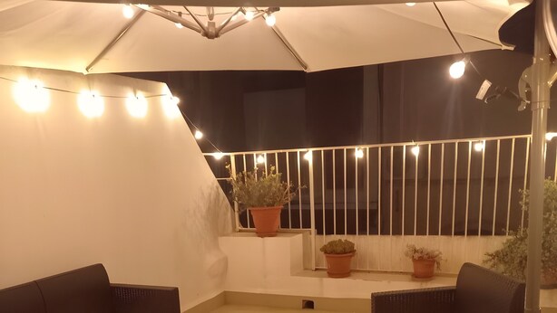 Eine Dachterrasse mit Gartenmöbeln, einem großen Sonnenschirm und Topfpflanzen.