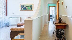 Ein modernes Wohnzimmer mit einer Couch, einem Glastisch, einem Bild an der Wand, einer Nähmaschine auf einem Holztisch und einer Heizung.