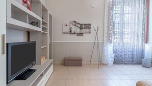 Ein modernes Wohnzimmer mit Flachbildfernseher, weißen Regalen, einer Bank und Kunstwerken an der Wand.