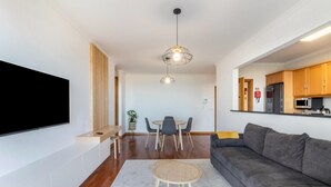 Una sala moderna con un televisor de pantalla plana, un sofá gris, una mesa de centro redonda y un comedor con una mesa y sillas.