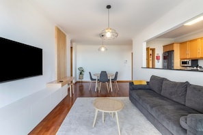 Un salon moderne doté d’un téléviseur à écran plat, d’un canapé gris, d’une table basse ronde et d’un coin repas avec une table et des chaises.