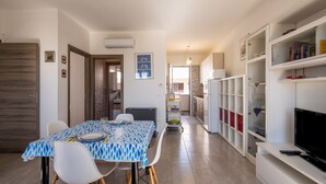 A modern kitchen with white cabinets, a dining area with a blue patterned tablecloth, and a TV on a white stand. - Holiday Home "Vista Mare Marittima di Diso" with Terrace & Wi-Fi (Marittima)
