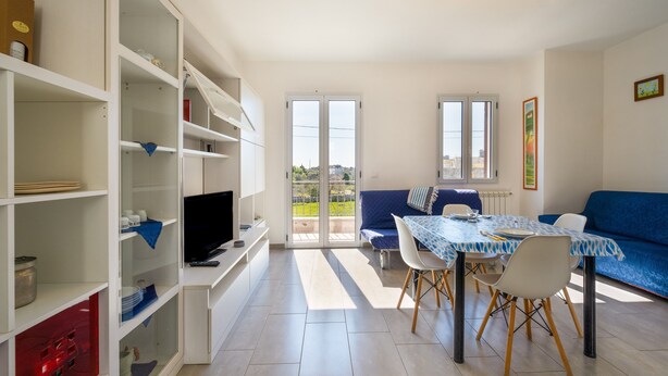 A modern living room with a dining area, built-in shelving, a television, and a view through glass doors. - Holiday Home "Vista Mare Marittima di Diso" with Terrace & Wi-Fi (Marittima)