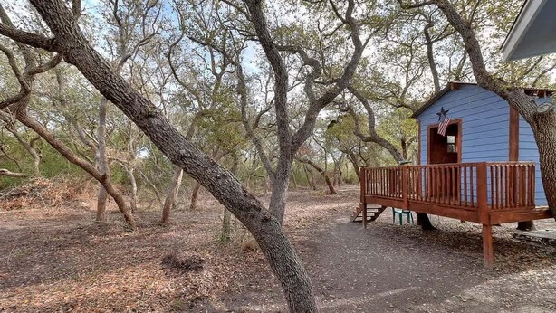 A rustic cabin with a wooden deck, surrounded by trees.