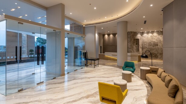 A modern lobby with a curved ceiling, glass walls, a reception desk, a sofa, and a yellow chair. - Holiday Inn Katra Vaishno Devi by IHG (Reasi)