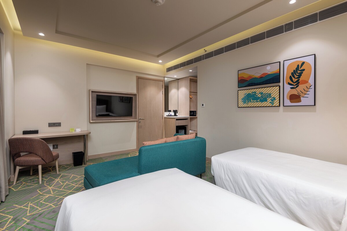 Habitación de hotel con dos camas, un escritorio, una silla y un televisor.