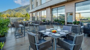 A rooftop dining area with tables and chairs, large windows, and potted plants. - Holiday Inn Katra Vaishno Devi by IHG (Reasi)