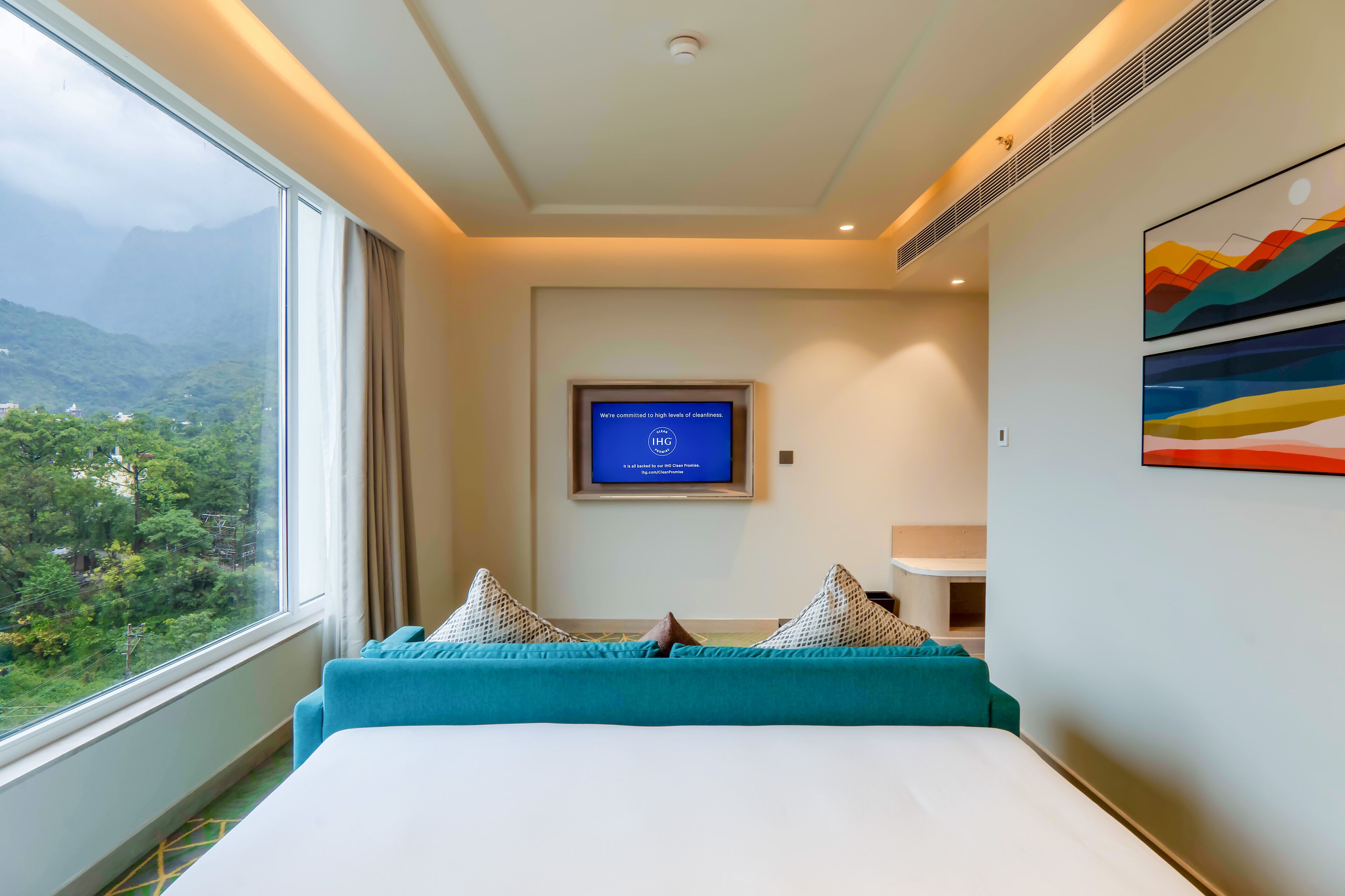 Quarto de hotel com uma cama grande, uma televisão fixada na parede e vista para uma paisagem montanhosa através de uma janela ampla.