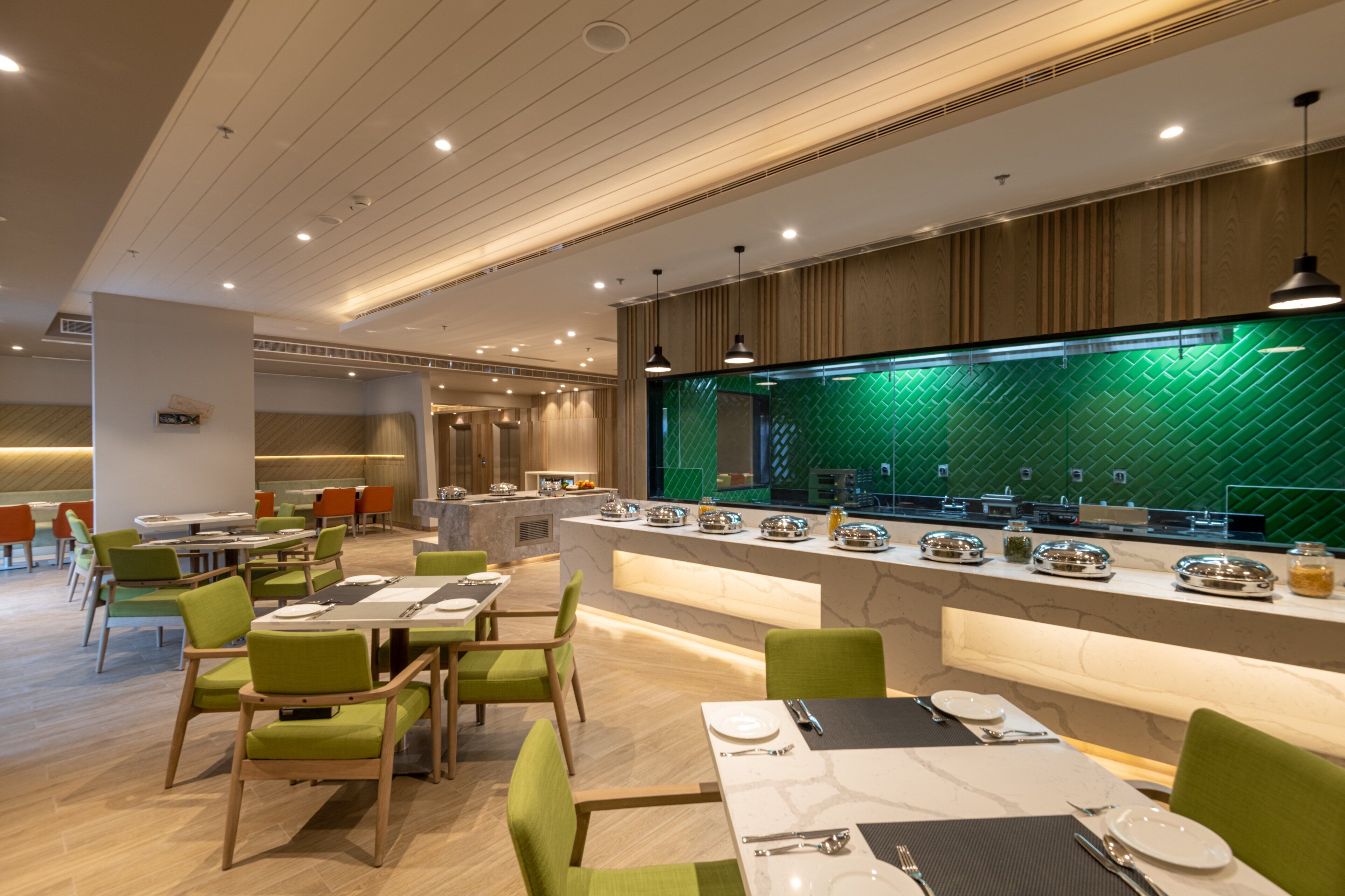 A modern restaurant with green chairs and a green-tiled backsplash.