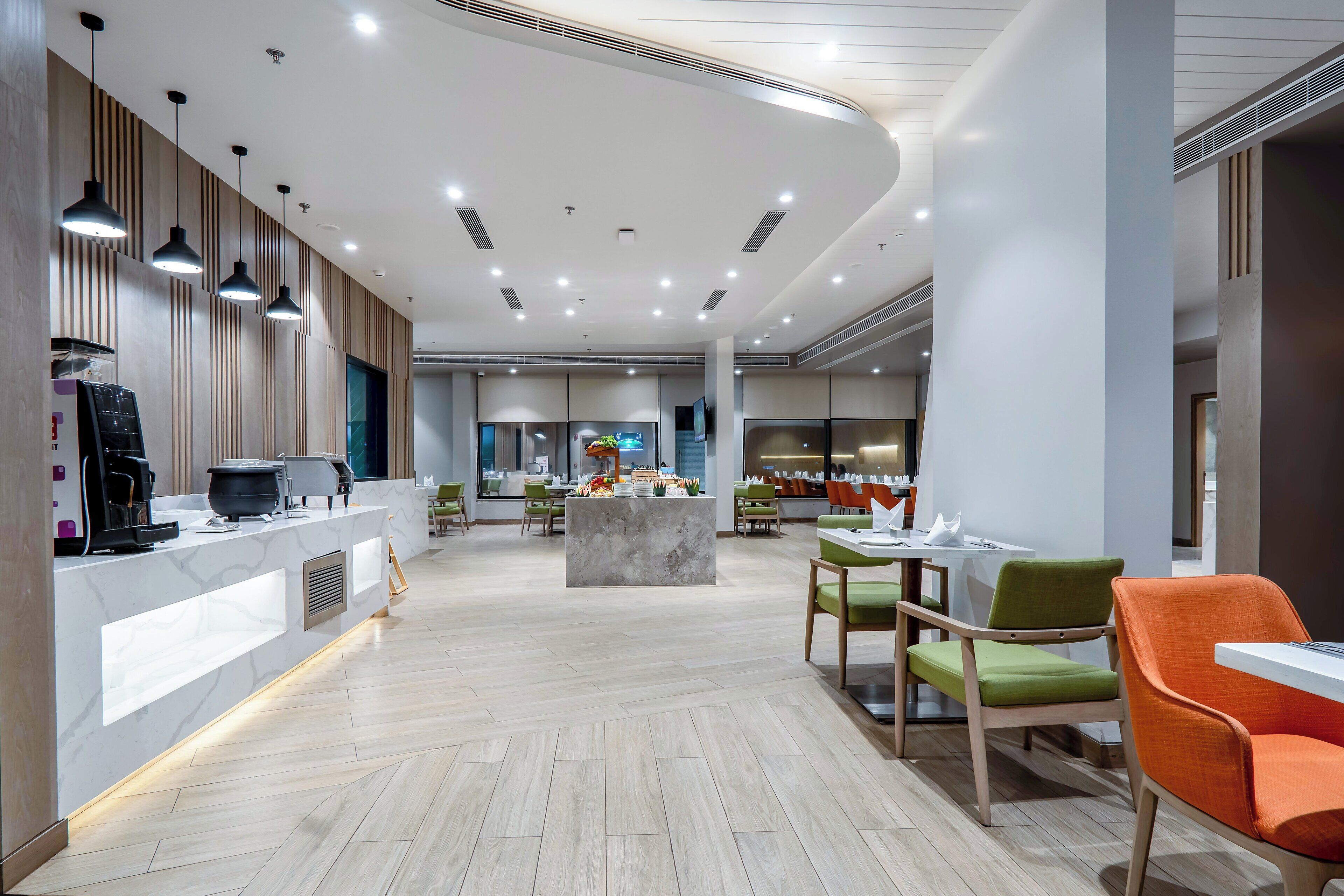 A modern hotel lobby with a central island, seating area, and a kitchen counter.