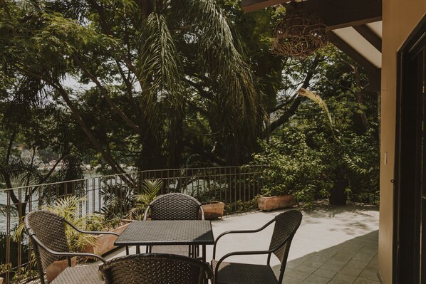 An outdoor patio with wicker furniture, a view of a body of water, and lush greenery.