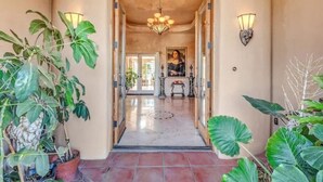 A hallway with a chandelier, potted plants, and a painting on the wall. - Hacienda Foothills Mansion (Tucson)