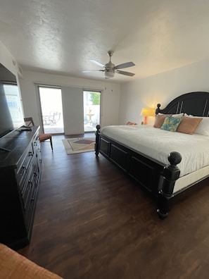 Quarto com cama, penteadeira, ventoinha no teto e vista para o exterior.