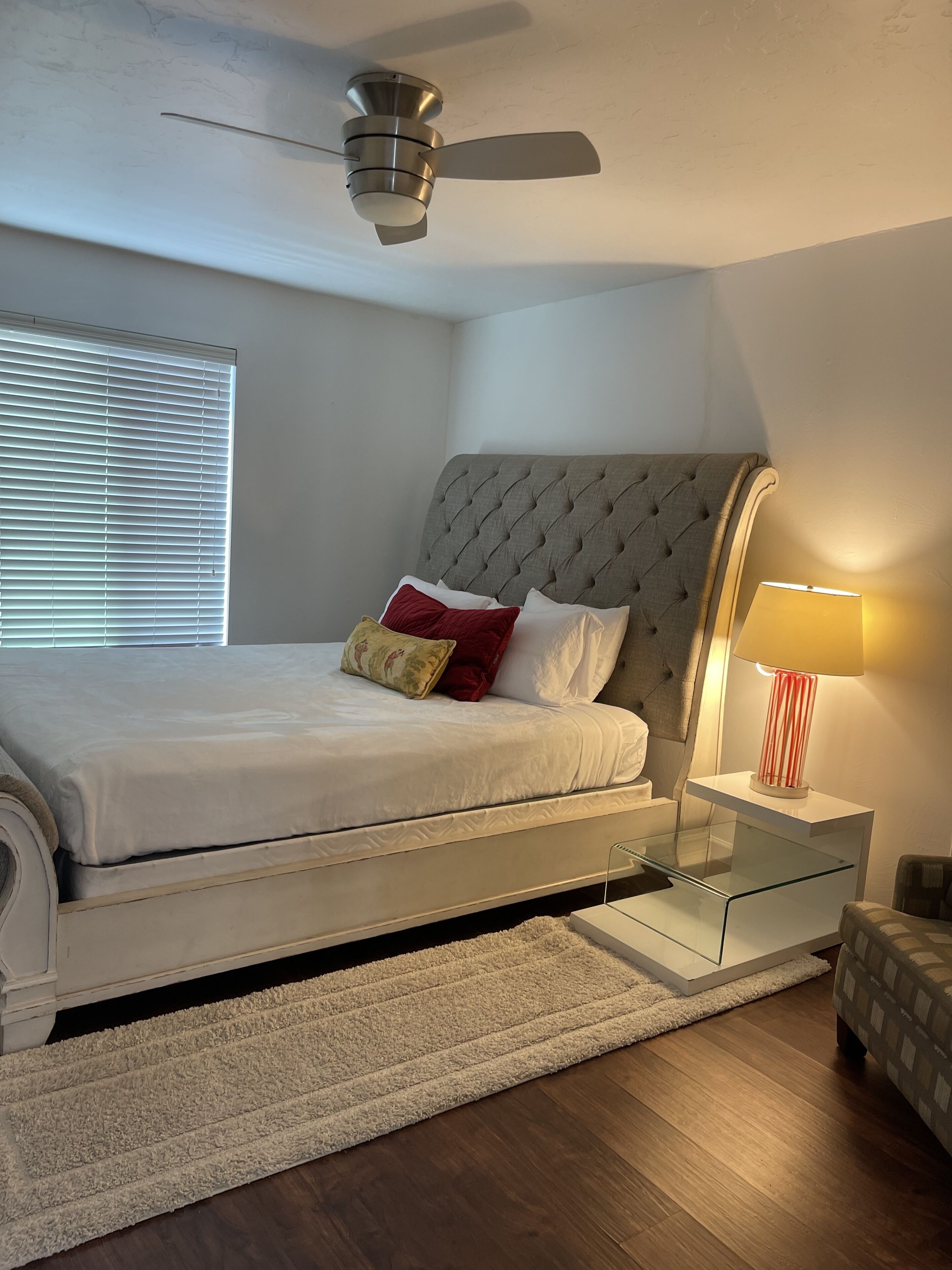 Een slaapkamer met een bed, een plafondventilator, een bedlampje en een nachtkastje.