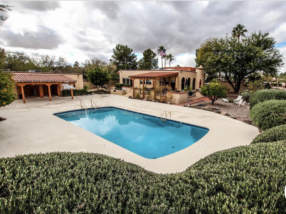 Une piscine avec une terrasse carrelée, un patio couvert et un bâtiment doté d’un toit en tuiles.