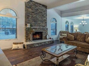 A living room with a stone fireplace, a glass coffee table, and a brown sofa.