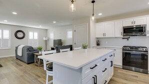 Une cuisine moderne avec des meubles blancs, un grand îlot central, des appareils en acier inoxydable et des luminaires suspendus.