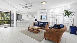 Un amplio espacio habitable con un ventanal grande, un ventilador de techo y una cocina al fondo.