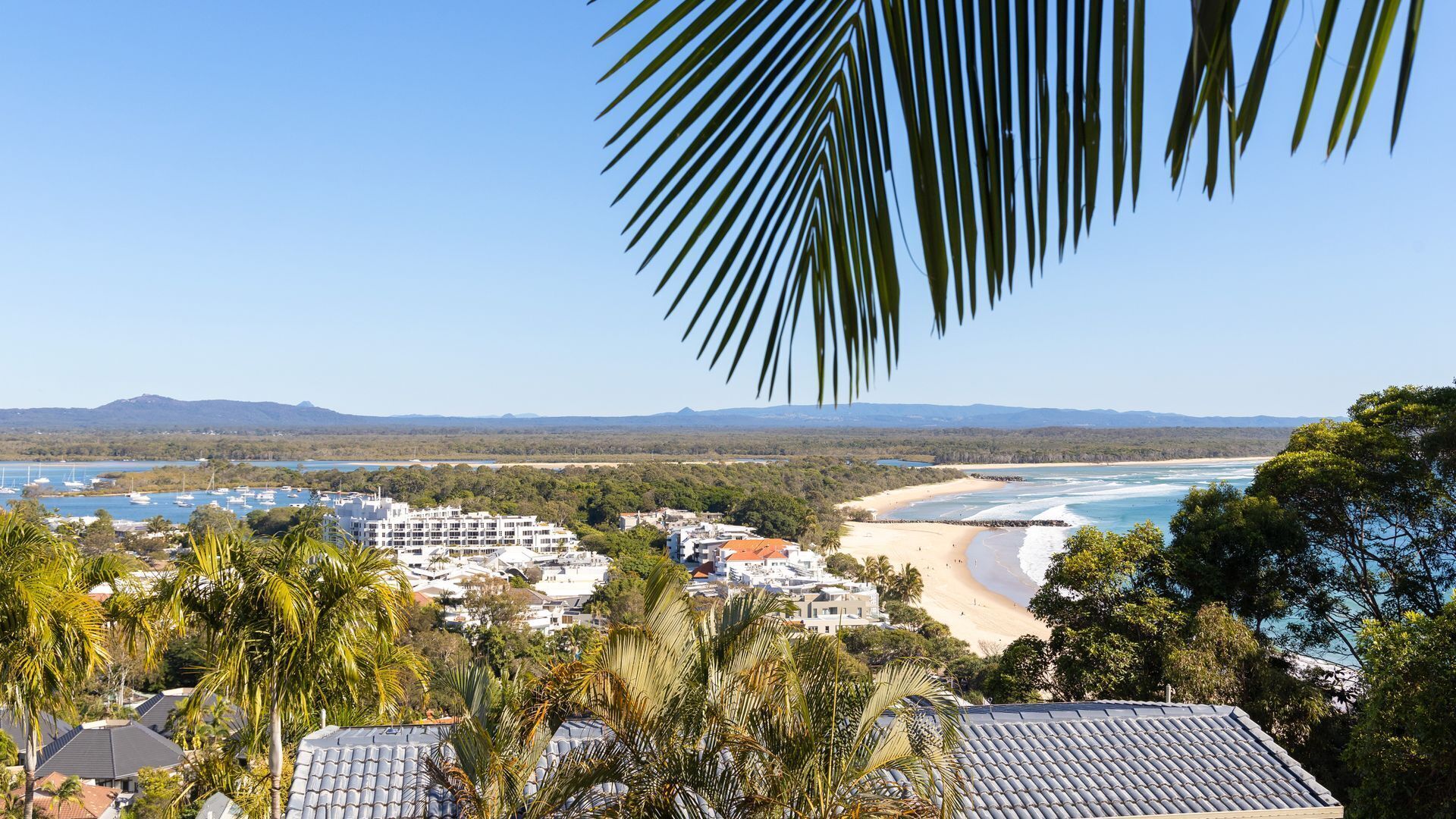 A coastal town with beachfront properties, a beach, and a view of the ocean and distant mountains.