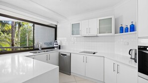 Una cocina moderna con armarios blancos, lavavajillas, estufa y cafetera.